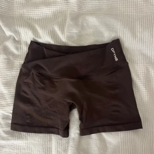 Bruna träningstights-shorts från DFYNE - Snygga bruna träningstights-shorts från DFYNE med hög midja och ribbad linning. Materialet är mjukt och stretchigt, perfekt för gymmet eller andra sportaktiviteter. Logga på både fram- och baksidan av linningen. Modellen är tight och sitter skönt på kroppen.