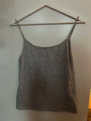 Grå linnetopp med smala axelband - Säljer en enkel och stilren grå linnetopp med smala axelband. Toppen har en rak passform och är tillverkad i mjuk bomull, perfekt för varma dagar. Den neutrala grå färgen gör den lätt att matcha med olika outfits.