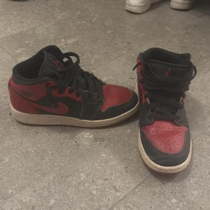 Nike Air Jordan 1 Bred sneakers - Säljer ett par klassiska Nike Air Jordan 1 i färgen Bred med svart och rött skinn, svarta snören och röd yttersula. Ikonisk siluett med rund tå och perforerad tåbox. Perfekta för dig som gillar streetwear och vill sticka ut med en tidlös sneaker.