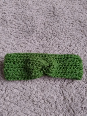 Grönt virkat pannband med twist - Snyggt handgjort virkat grönt pannband som jag gjort själv . Det har en twistad detalj framtill som ger en cool look och sitter skönt runt huvudet. Perfekt för att hålla öronen varma och samtidigt se trendig ut.