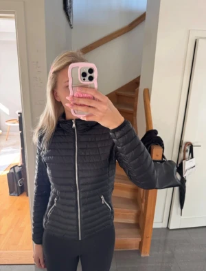 Svart dunjacka från Colmar - Säljer en svart dunjacka från Colmar Originals med huva och snygga quiltade detaljer. Jackan har silverfärgade dragkedjor framtill och på fickorna, samt Colmar-logga på ärmen. Perfekt för dig som vill ha en lätt och stilren jacka med grym passform.Storleken är 40 