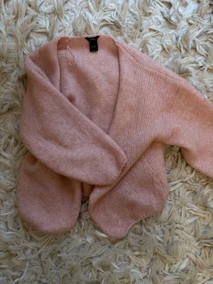 Ljusrosa stickad kofta från Lindex - Supermysig ljusrosa stickad kofta från Lindex i storlek XS/S. Koftan har en loose passform, långärmade ärmar och är öppen framtill utan knappar. Perfekt att slänga över en topp för en chill look. Materialet är mjukt och fluffigt.