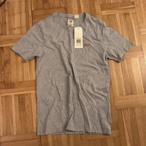 Grå Levi's t-shirt XS - Snygg grå t-shirt från Levi's i klassisk modell med rund hals och korta ärmar. Diskret Levi's-logga i rött på bröstet ger en clean look. Tillverkad i mjuk bomull som känns skön mot huden. Perfekt för dig som gillar enkel och stilren streetwear.