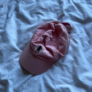 Rosa keps från Grizzly - Säljer en rosa keps från Grizzly med den klassiska björnen broderad framtill. Kepsen är i mjuk bomull och har justerbar rem baktill för perfekt passform. Perfekt accessoar för en chill streetwear-look.