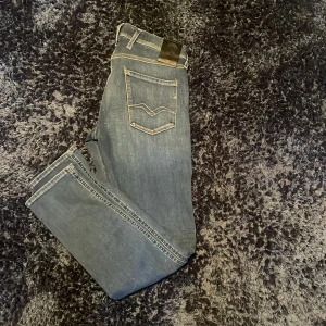 Replay Anbass blå jeans slim fit - Säljer ett par snygga Replay Anbass jeans i blå tvätt med klassiska fem fickor och coola detaljer på bakfickorna. Jeansen har slim passform, normal midja och är tillverkade i stretchigt denim för skön komfort. Perfekt för dig som gillar stilrena och moderna jeans.