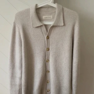 Beige stickad kofta från Pier One - Snygg beige stickad kofta från Pier One i storlek S, med klassisk krage och stora knappar framtill. Koftan har långärmad passform och är gjord i mjukt material som känns skönt mot huden. Perfekt att slänga över en t-shirt för en chill look. Nypris ligger på 500kr.