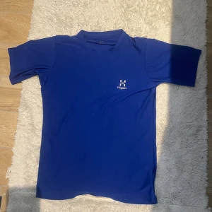 Blå Haglöfs t-shirt träningströja - Snygg blå t-shirt från Haglöfs med diskret logga på bröstet. Klassisk passform och korta ärmar, perfekt för träning eller chill. Materialet är lätt och andas, vilket gör den skön att ha på sig under aktiva dagar. Helt ny