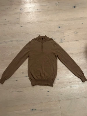 Brun half zip - Snygg brun half zip från J.Linderberg. Tröjan har långärmade och ribbade muddar vid ärmslut och nederkant. Perfekt för dig som gillar en enkel och stilren look med lite extra detalj vid halsen. Enbart använd ett fåtal gånger.