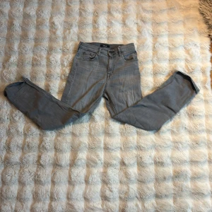 Grå jeans från Replay Thad - Säljer ett par grå jeans från Replay, modell Thad. De har klassisk femficksdesign, raka ben och snygga detaljer på bakfickorna. Jeansen är tillverkade i mjukt denimtyg och har en neutral grå färg som passar till det mesta.