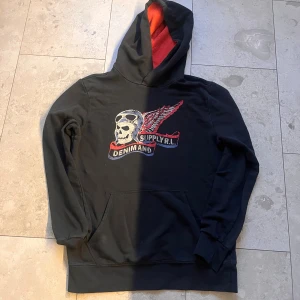 Svart hoodie Denim & Supply Ralph Lauren - Svart hoodie från Denim & Supply Ralph Lauren med röd insida i huvan och coolt tryck med döskalle, pilotglasögon och vingar på bröstet. Tröjan har känguruficka och långa ärmar. Materialet är mjuk bomull, perfekt för chill dagar.