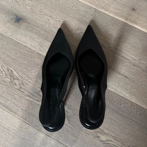 Svarta pumps med spetsig tå Stradivarius - Snygga svarta pumps från Stradivarius med spetsig tå och öppen häl. Skorna har hög klack och en elegant, smal siluett. Materialet är slät syntet med matt finish. Perfekta för dig som gillar stilrena och trendiga skor med attityd. (de var för stora för mig)