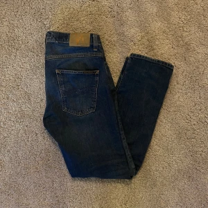 Mörkblå Nudie Jeans  W30 L30 Grim Tim - Säljer ett par mörkblå jeans från Nudie Jeans Co i storlek W30 L30 modell Grim Tim. Jeansen har klassisk femficksdesign, raka ben och snygga kontrastsömmar. Jeansen är i i bra skick.