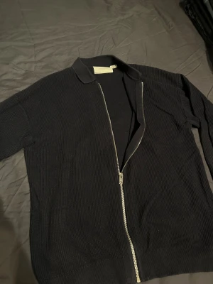 Mörkblå stickad cardigan  - Svart stickad cardigan jacka från Jack & Jones med grov ribbad struktur, klassisk krage och hel dragkedja framtill. Perfekt för lager-på-lager och chill stil. Långärmad modell. Kan användas som en vanlig tröja eller lätt tunn jacka. Ny pris 699. 