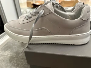 Grå sneakers från Filling Pieces - Snygga grå sneakers från Filling Pieces med rund tå och platt vit sula. Skorna har snörning och är tillverkade i mjuk mocka som ger en lyxig känsla. Perfekt för dig som gillar stilrena och minimalistiska sneakers med premiumkänsla. Använda 1 gång bara