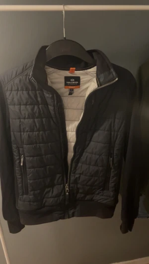 Svart quiltad jacka Parajumpers Y-M - Svart quiltad jacka från Parajumpers med broderad patch på ärmen. Jackan har dragkedja framtill, två fickor med dragkedja och ribbade muddar. Materialet är polyester och fleece, perfekt för kyliga dagar. Snygg och sportig look med klassisk Parajumpers-detalj.