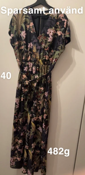 Blommig jumpsuit med knytband - Snygg jumpsuit med blommigt mönster i mörka och ljusa färger. Jumpsuiten har v-ringning, korta ärmar och ett knytband i midjan som ger en fin siluett. Perfekt för dig som gillar romantiska och färgglada plagg.🌸Sparsamt använd. Har ”skärp”. Storlek 40