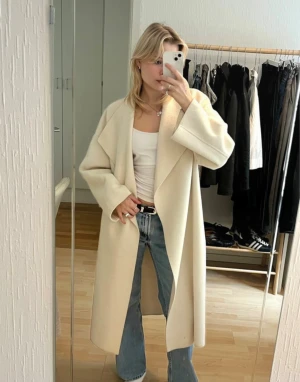 Oversized beige kappa från Nelly x Bianca - Säljer en oversized beige kappa från Nellys colab med Bianca, med breda slag och bälte i midjan. Jackan har lång ärm och en clean, minimalistisk look. Materialet är mjukt och känns lyxigt, perfekt för dig som gillar stilrena vibes och vill ha en snygg layering-piece. Kappan har små tecken på användning (se bild)