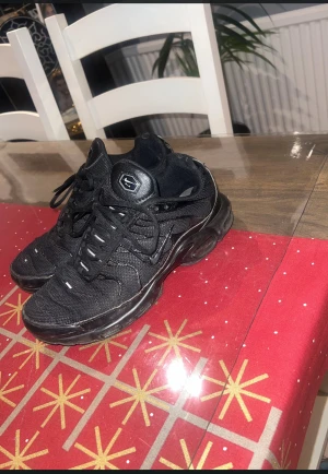 Svarta Nike Air Max Plus TN sneakers - Säljer ett par svarta Nike Air Max Plus TN sneakers med mesh och syntetdetaljer. Skorna har den klassiska Tn-loggan bak, vågiga paneler och en chunky sula med synliga luftbubblor. Perfekta för dig som gillar streetwear och vill ha en riktigt fet siluett.