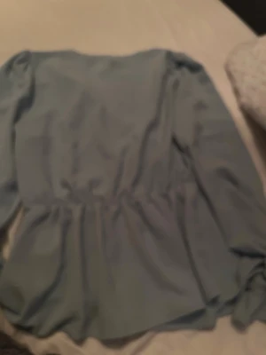 Ljusblå blus med spets från Vero Moda - Säljer en ljusblå blus från Vero Moda med v-ringad hals och dekorativ spetskant. Blusen har lång ärm och lätt rynkade detaljer vid midjan för en snygg siluett. Perfekt för dig som gillar stilrena och feminina plagg.