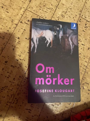 Om mörker - En pocketbok med ett mystiskt omslag där vita hästar syns i ett mörkt stall. Titeln och författarnamnet är tryckta i starkt rosa, vilket ger ett modernt och tilltalande intryck. Perfekt för dig som gillar böcker med djup och visuellt spännande omslag.