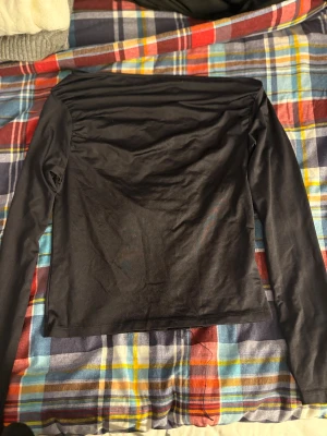 Svart långärmad offshoulder topp - Säljer en svart långärmad topp med offshoulder-design. Toppens stil är enkel och clean, med en rak passform och slät yta. Perfekt för dig som gillar minimalistiska looks och vill ha en basic topp som funkar till många olika outfits.