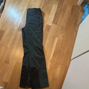 Mörkgrå skidbyxor från Peak Performance - Snygga mörkgrå skidbyxor från Peak Performance i storlek XS. Byxorna har dragkedjor vid bensluten och utrustade med Recco. Perfekta för skidåkning och utomhusaktiviteter. 