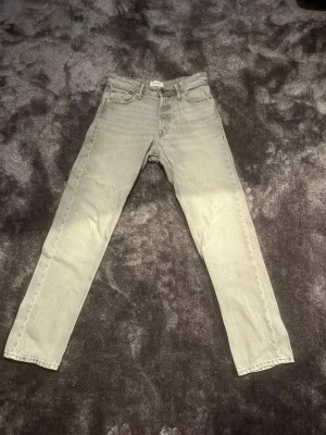 Grå loose fit jeans från Jack & Jones - Säljer ett par grå jeans från Jack & Jones, modell Loose/Chris. De har en loose passform med raka ben och klassisk femficksdesign. Jeansen är tillverkade i slitstarkt bomullsmaterial och har knappgylf samt bälteshällor.