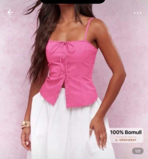 Rosa linnetopp med knyt och knappar - Säljer en söt rosa linnetopp i 100% bomull med smala axelband, knyt framtill och knappar längs hela framsidan. Toppen har en figurnära passform och är perfekt för varma dagar. Supersnygg att styla med kjol eller jeans!