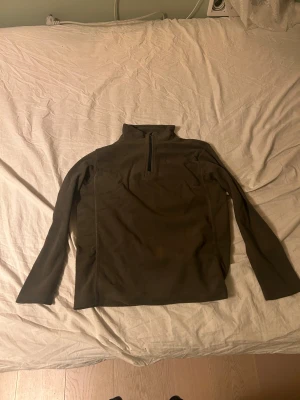 Mörkbrun fleece-tröja med half zip - Säljer en mörkbrun fleece-tröja med halv dragkedja och hög krage. Tröjan har långärmad passform och är perfekt för kyliga dagar. Materialet är mjukt och värmande, och modellen är normal i passningen. Enkel och stilren design utan synliga loggor.