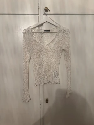 Vit spetsblus med v-ringning - Säljer en vit blus från Gina tricot i genombruten spets med blommigt mönster. Toppen har v-ringad hals och långa ärmar, perfekt för dig som gillar romantisk och feminin stil. Sitter snyggt och är lätt att matcha med jeans eller kjol.