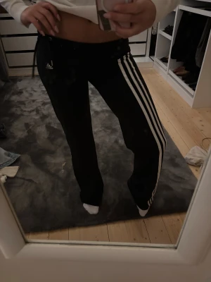 U21 adidasmjukis Lågmidjade  - Säljer ett par svarta Adidas mjukisbyxor med klassiska vita ränder längs sidorna och logga framtill. Byxorna har snörning i midjan och är lågmidjade med en loose passform. Perfekta för chill eller träning, riktigt sköna och snygga.