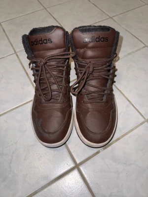 Adidas med foder - Säljer ett par bruna Adidas boots med svart foder och svarta detaljer. Dem är bara använda en halv vinter säsong så dem är nästan nya. Inköpta för 1200kr