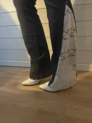 Svarta jeans med spetsdetaljer - Unika svarta jeans med breda spetsinsatser i vitt längs utsidan av benen. Modellen har en rak passform med bootcut och coola slitningar framtill.  Perfekt för dig som vill sticka ut med din stil. Byxorna är från märket R-jeans, men det är vi på TÄFmade som sydd om dom!  Midjan är 33 cm, Innerben är 73 cm! 