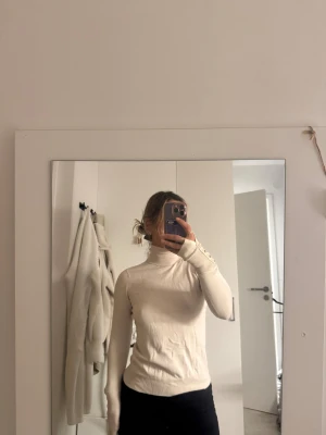 Beige polotröja med pärlknappar - Säljer en beige polotröja med lång ärm och snygga pärlknappar på mudden. Tröjan är figurnära och har en mjuk, stretchig känsla. Perfekt för lager-på-lager och passar till allt. Stilren och enkel att matcha.