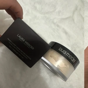 Laura Mercier Translucent Loose Setting Powder - Translucent Loose Setting Powder från Laura Mercier i en rund plastburk med svart lock. Pudret är ljust och transparent, perfekt för att fixera din makeup och ge en matt finish. Förpackningen innehåller 29g och kommer i originalkartong.