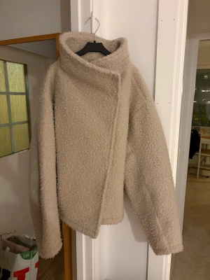 Beige teddyjacka från Gina Tricot - Säljer en beige teddyjacka från Gina Tricot i storlek S. Jackan har en oversized krage, asymmetrisk knäppning med knapp och är tillverkad i mjukt teddy-material. Perfekt för dig som gillar en chill och cozy stil med lite edge.