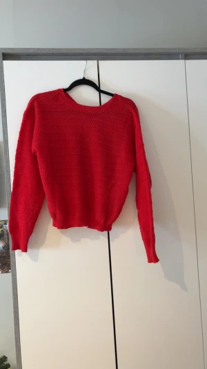 Röd stickad tröja med rosett från SHEIN - Säljer en röd stickad tröja från SHEIN i storlek S. Tröjan har långärmade ärmar, rund hals och en stor rosett bak i nacken som ger en gullig touch. Materialet är 100% polyester och strukturen är ribbad med diskreta horisontella ränder.