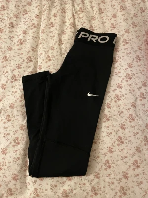 Nike Pro svarta leggings strl L - Svarta Nike Pro leggings med bred resår i midjan och vit logga på benet. Snygg och sportig design som sitter tight och är perfekta för träning. Materialet är stretchigt syntet som andas och ger bra rörelsefrihet. Barn storlek 