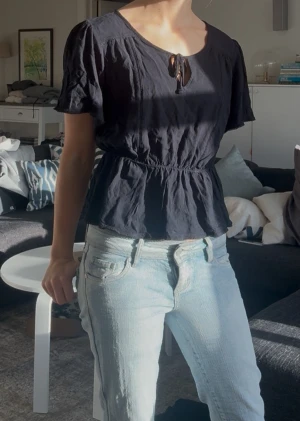 Svart blus med knyt och volang - Säljer en svart blus med korta ärmar och rund halsringning med söt knytning framtill. Köp i USA för ca 400kr men säljer nu för 100. Den är knappt använd och i storlek S