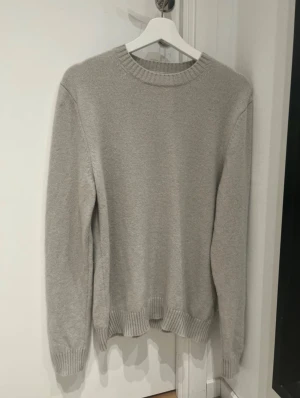 Grå stickad tröja från Samsøe Samsøe - Snygg grå stickad tröja från Samsøe Samsøe i storlek M. Tröjan har rund hals, ribbade muddar vid ärmslut och nederkant samt långärmad passform. Perfekt för dig som gillar enkel och clean stil med skandinavisk vibe.