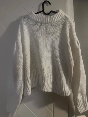 Vit stickad polotröja - Mysig vit stickad polotröja med bred ribbad krage och långa ärmar. Tröjan har en loose passform och ribbade detaljer vid nederkant och ärmslut. 