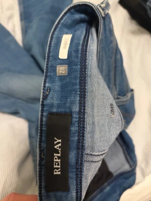 Replay Anbass jeans ljusblå, storlek 28 - Säljer ett par Replay Anbass jeans i ljusblå tvätt med klassisk femficksdesign och snygga slitningar. Modellen har smal passform och raka ben, med detaljerade sömmar på bakfickorna. Materialet är mjukt jeans och byxorna har dragkedja i gylfen. 