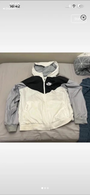 Nike vindjacka  svart/vit/grå - Nike vindjacka i storlek med huva och dragkedja. Jackan har en snygg färgblockad design i svart, vit och ljusgrå. Två sidofickor med dragkedja och Nike-logga på bröstet. Perfekt för dig som gillar sportig och clean stil.