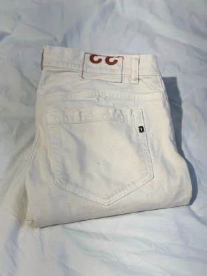 Vita jeans från Dondup med slim passform - Säljer ett par vita jeans från Dondup med klassisk femficksdesign och slim passform. Jeansen har diskreta slitningar och en liten dondup-logga på bakfickan. Perfekta för dig som vill ha en clean och stilren look.