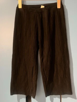 Svarta ribbade leggings - Snygga svarta leggings med ribbad struktur och elastisk midja. Modellen är croppad och har raka ben, vilket ger en trendig och avslappnad look. Perfekta att styla med oversized tröjor eller hoodies.