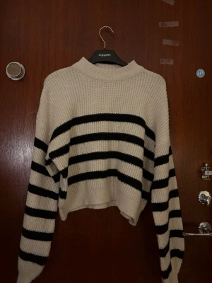 Randig stickad tröja från NLY Trend - Säljer en krämvit stickad tröja från NLY Trend med svarta horisontella ränder. Tröjan har en avslappnad passform, ribbad rund halsringning och långa ärmar. Perfekt för dig som gillar en casual och trendig look.