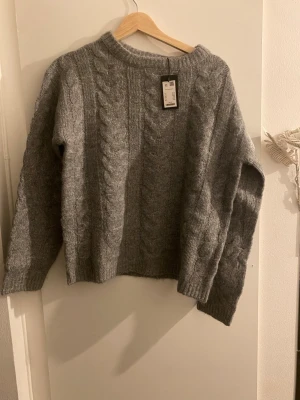 Grå kabelstickad tröja från H&M - Mysig grå stickad tröja. Tröjan har rund halsringning och långa ärmar. Perfekt för kyliga dagar och enkel att matcha med jeans eller kjol. Prislapp kvar ✨