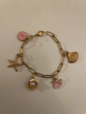 Guldigt berlockarmband  - Guld berlockarmband med fyra fina berlocker. Perfekt för dig som gillar strandvibbar och detaljer. Kedjan är i rostfritt stål.                               Tveka inte fråga om du har flera frågor 🌸💕