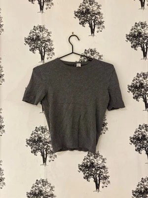 Mörkgrå croppad stickad topp - En enkel och stilren mörkgrå croppad topp med korta ärmar och rund hals. Stickad i mjukt material som ger en skön känsla. Perfekt att matcha med höga jeans eller kjol för en clean look. Den måste strykas!💓