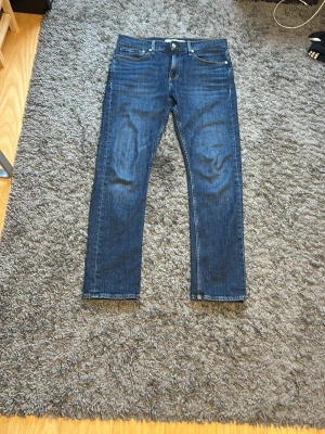 Mörkblå jeans från Calvin Klein - Asfeta mörkblå jeans från Calvin Klein Jeans med klassisk femficksmodell sopassform. Jeansen har raka ben och subtila slitningar vid knäna. Tillverkade i mjuk denim som ger en skön känsla och stilren look.  Utöver det bara använd ett fåtal gånger.